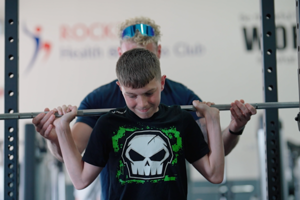 Boy lifting barbell on shoulders